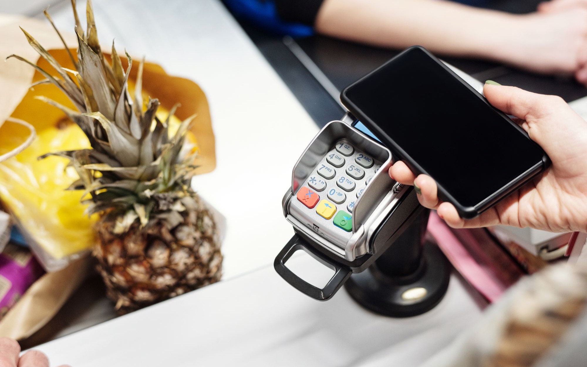 Hand hält ein Smartphone zum kontaktlosen Bezahlen an ein Kartenterminal an der Kasse