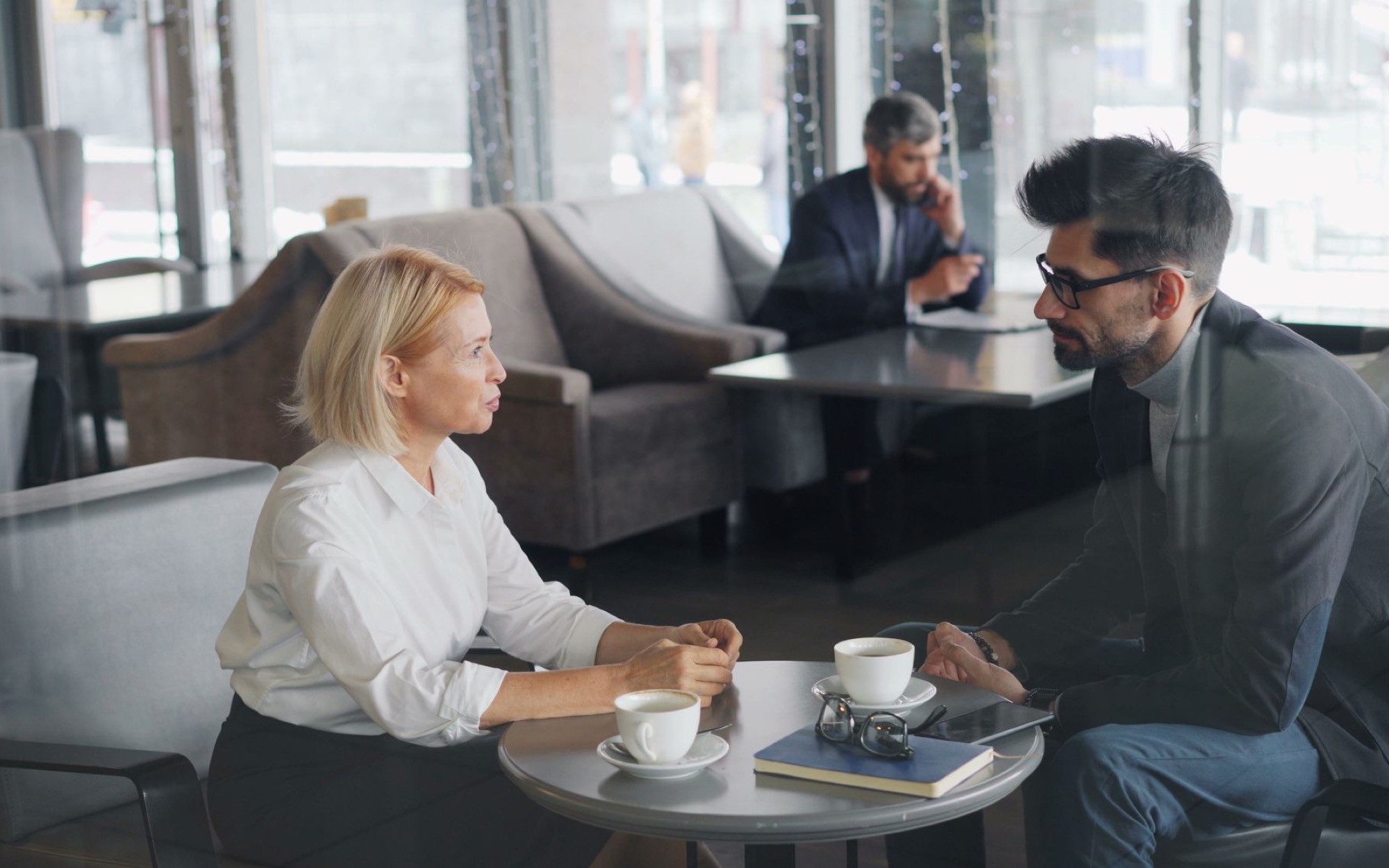 Frau und Mann im Gespräch an einem kleinen Tisch mit Kaffeetassen in einer Hotellobby