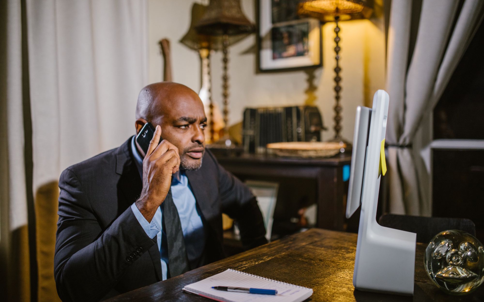 Mann im Anzug telefoniert konzentriert an einem Holzschreibtisch, vor ihm liegt ein Notizblock