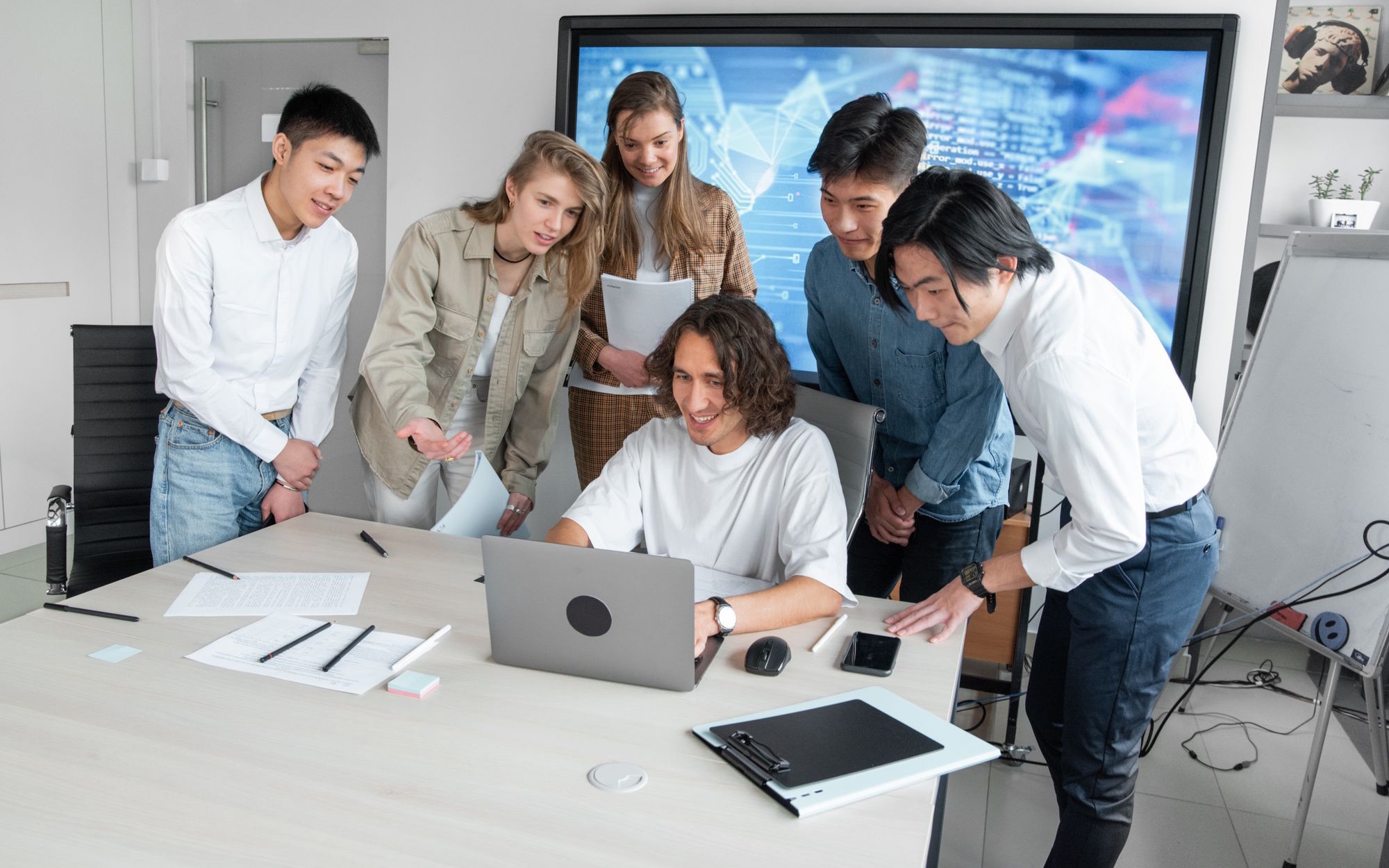 Mehrere Personen stehen um einen Schreibtisch und schauen gemeinsam auf einen Laptop