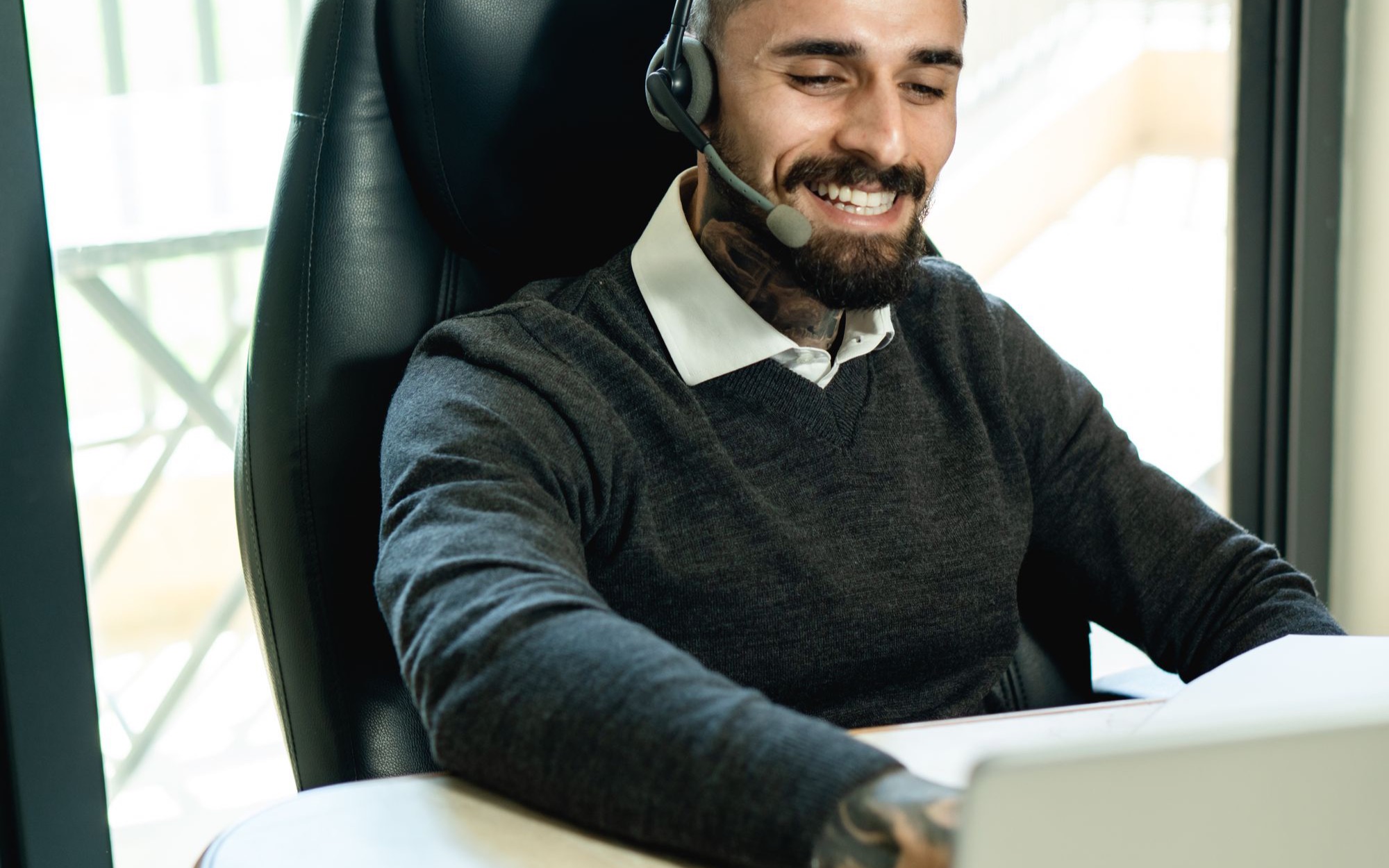 Lächelnder Mann mit Headset sitzt am Schreibtisch vor einem Laptop
