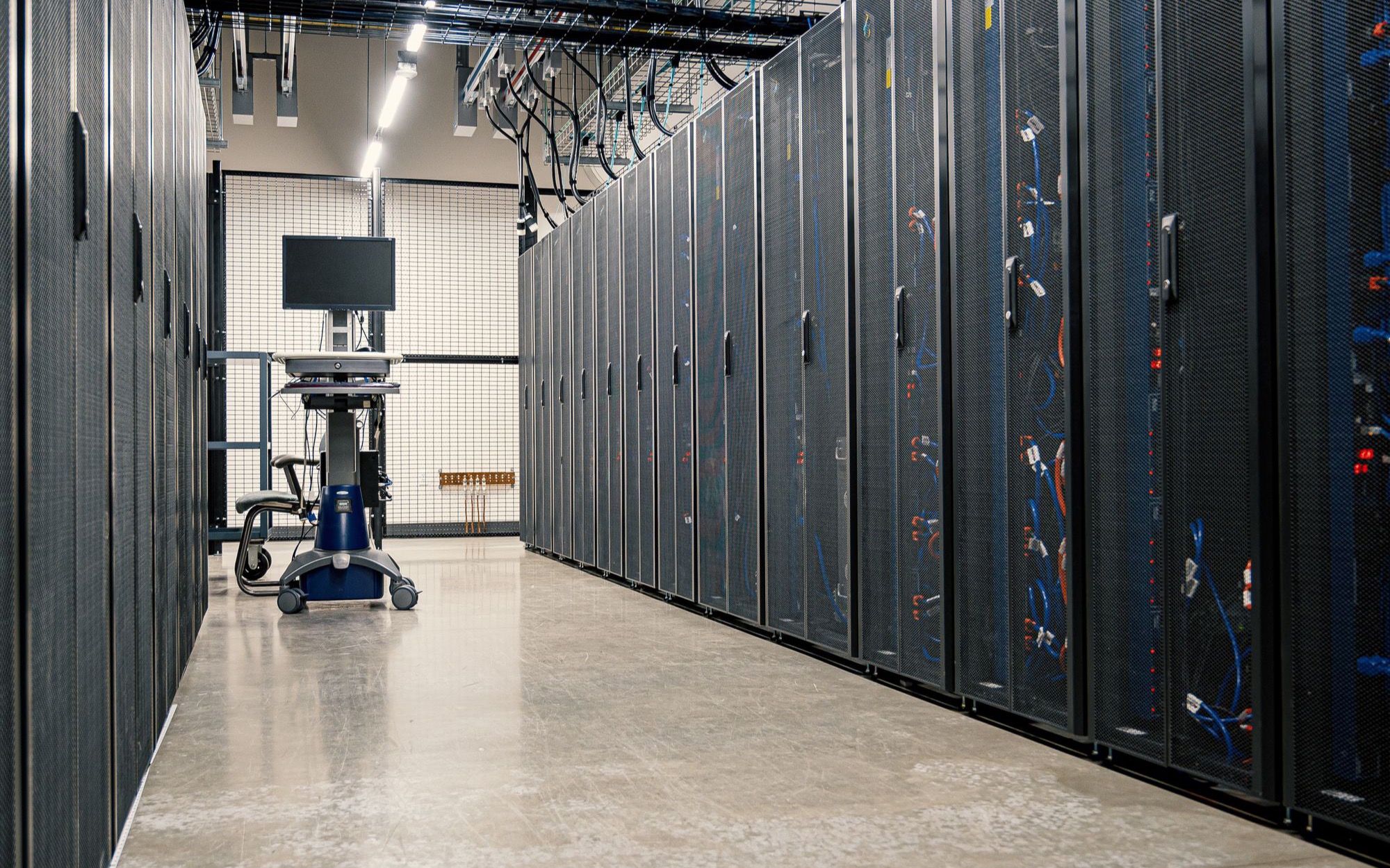 Langer Gang in einem Rechenzentrum zwischen schwarzen Serverschränken mit Kabeln