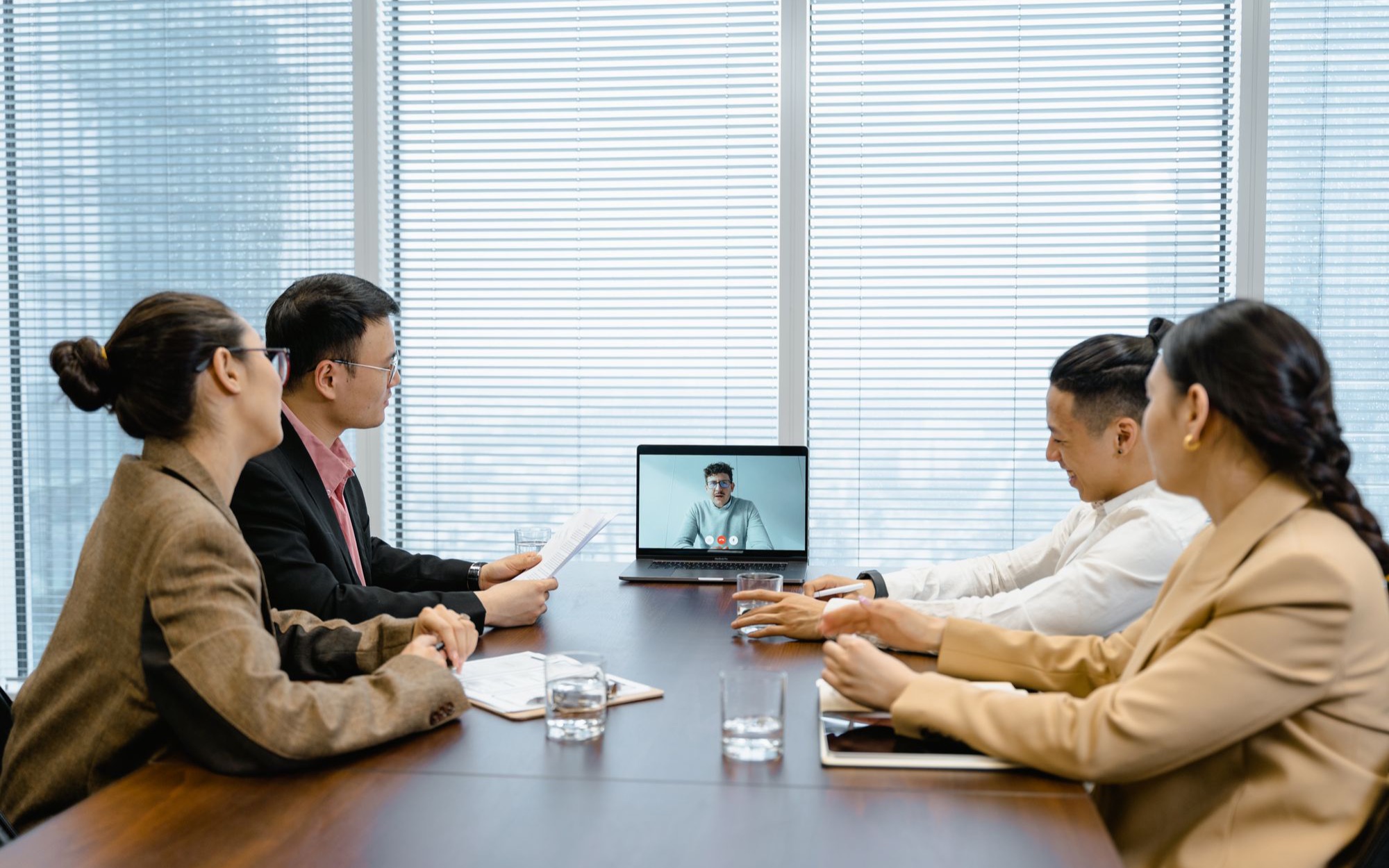 Vier Personen am Besprechungstisch sprechen mit einem Teilnehmer, der per Laptop zugeschaltet ist