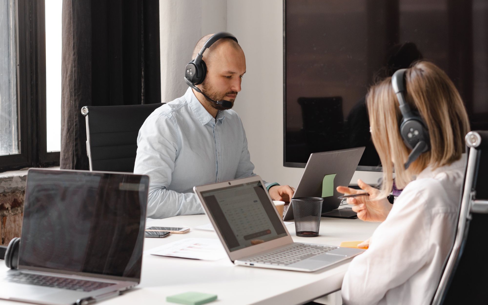 Mann und Frau mit Headsets arbeiten an Laptops an einem gemeinsamen Bürotisch