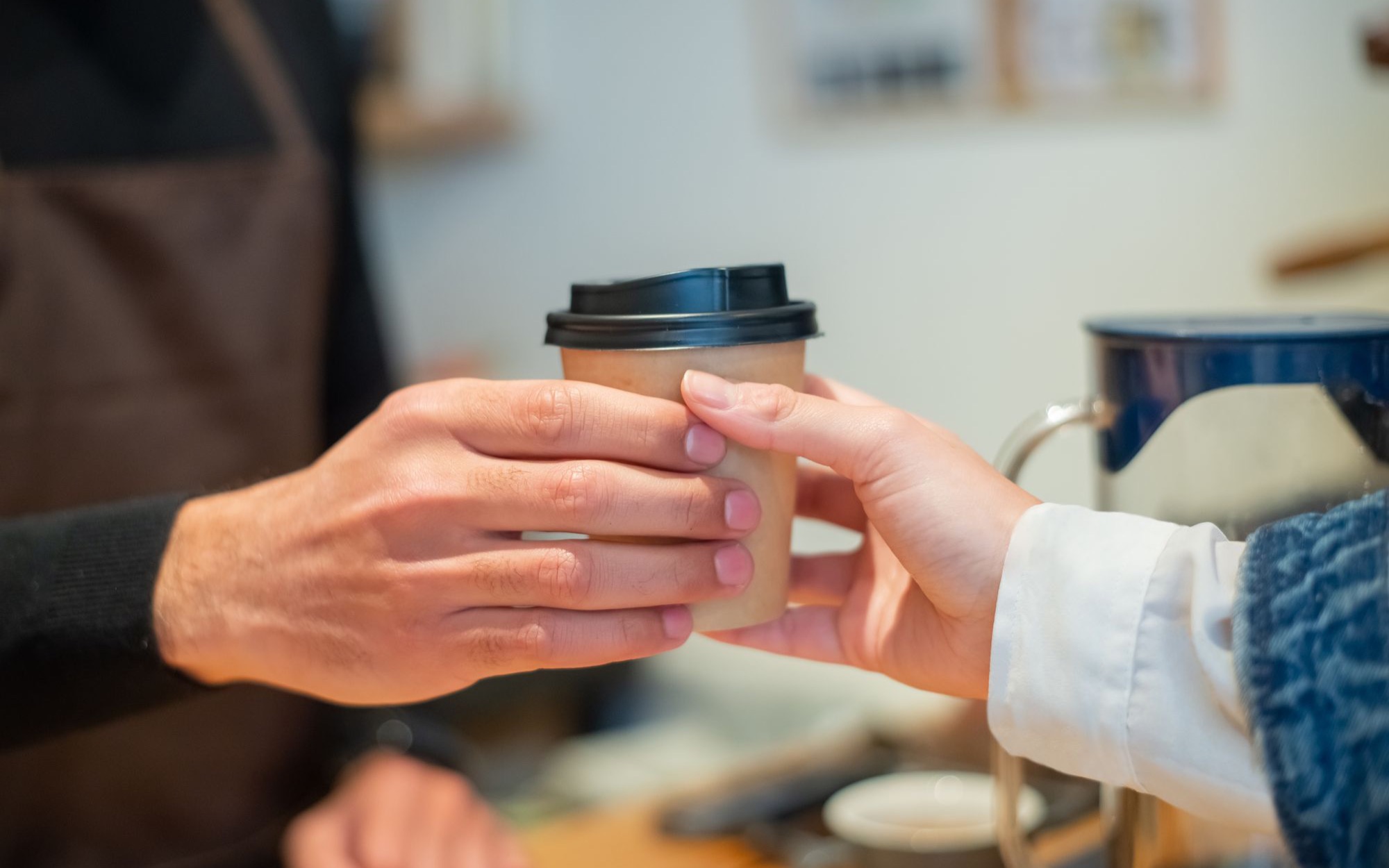 Hand reicht einen Kaffeebecher zum Mitnehmen über die Theke an eine Kundin